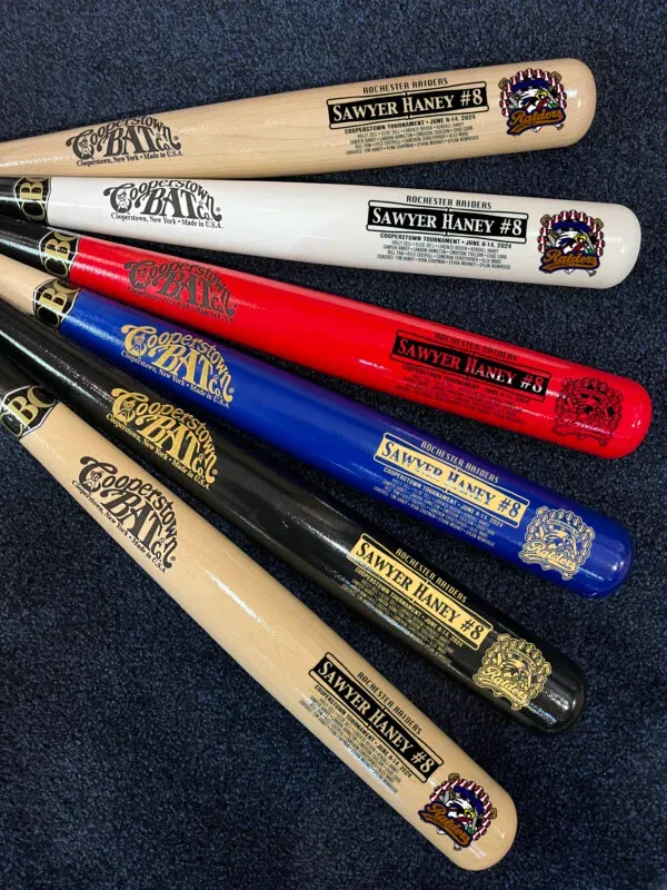 Six colorful baseball bats with Cooperstown tournament dates.